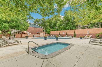 A small pool surrounded by a concrete patio and deck chairs.